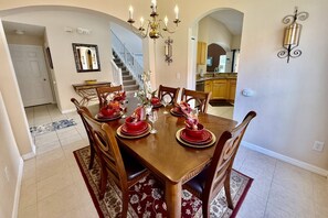 Une salle à manger avec une table en bois dressée pour six personnes, un lustre et un escalier menant à une autre pièce.