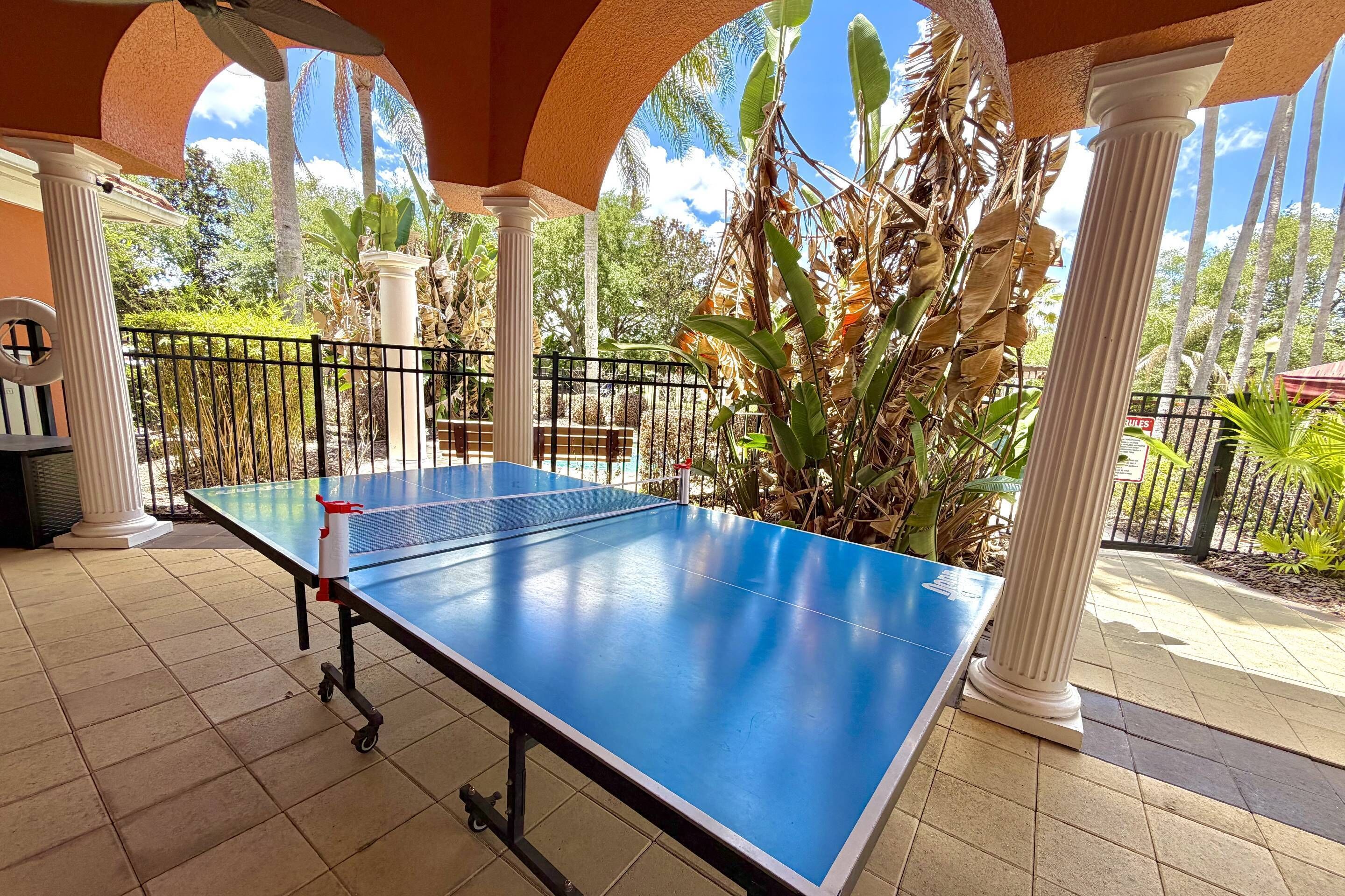 A ping pong table in an outdoor area with columns and a view of palm trees.