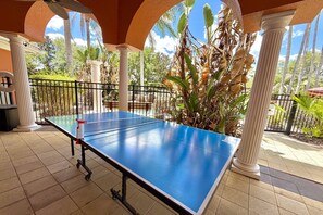 Ein Tischtennis-Tisch in einem Außenbereich mit Säulen und Blick auf Palmen.