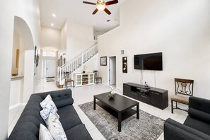 Ein geräumiges Wohnzimmer mit einer Couch, einem Couchtisch, einem Fernseher und einer Treppe, die zu einer weiteren Ebene führt.