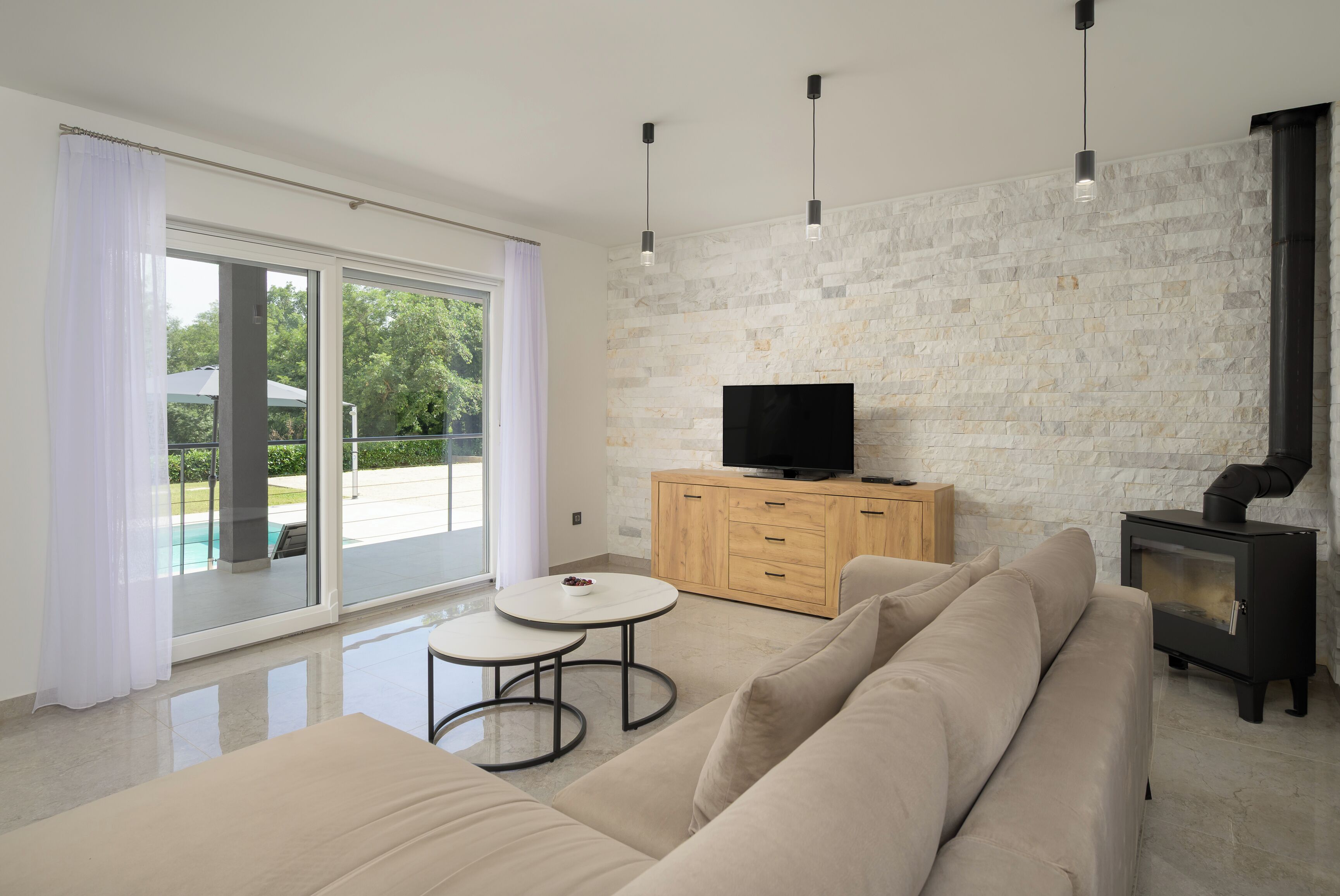 Un salon moderne avec un canapé, un téléviseur posé sur un meuble en bois et une porte vitrée donnant sur une piscine.