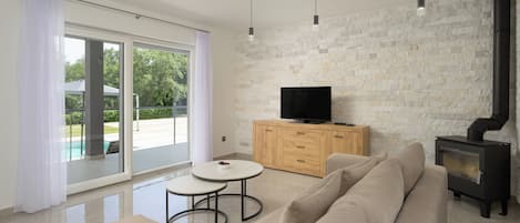 Un salon moderne avec un canapé, un téléviseur posé sur un meuble en bois et une porte vitrée donnant sur une piscine.