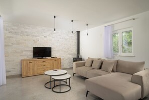 Ein modernes Wohnzimmer mit Steinwand, Flachbildfernseher, Holzschrank, beiges Sofa und rundem Tisch.
