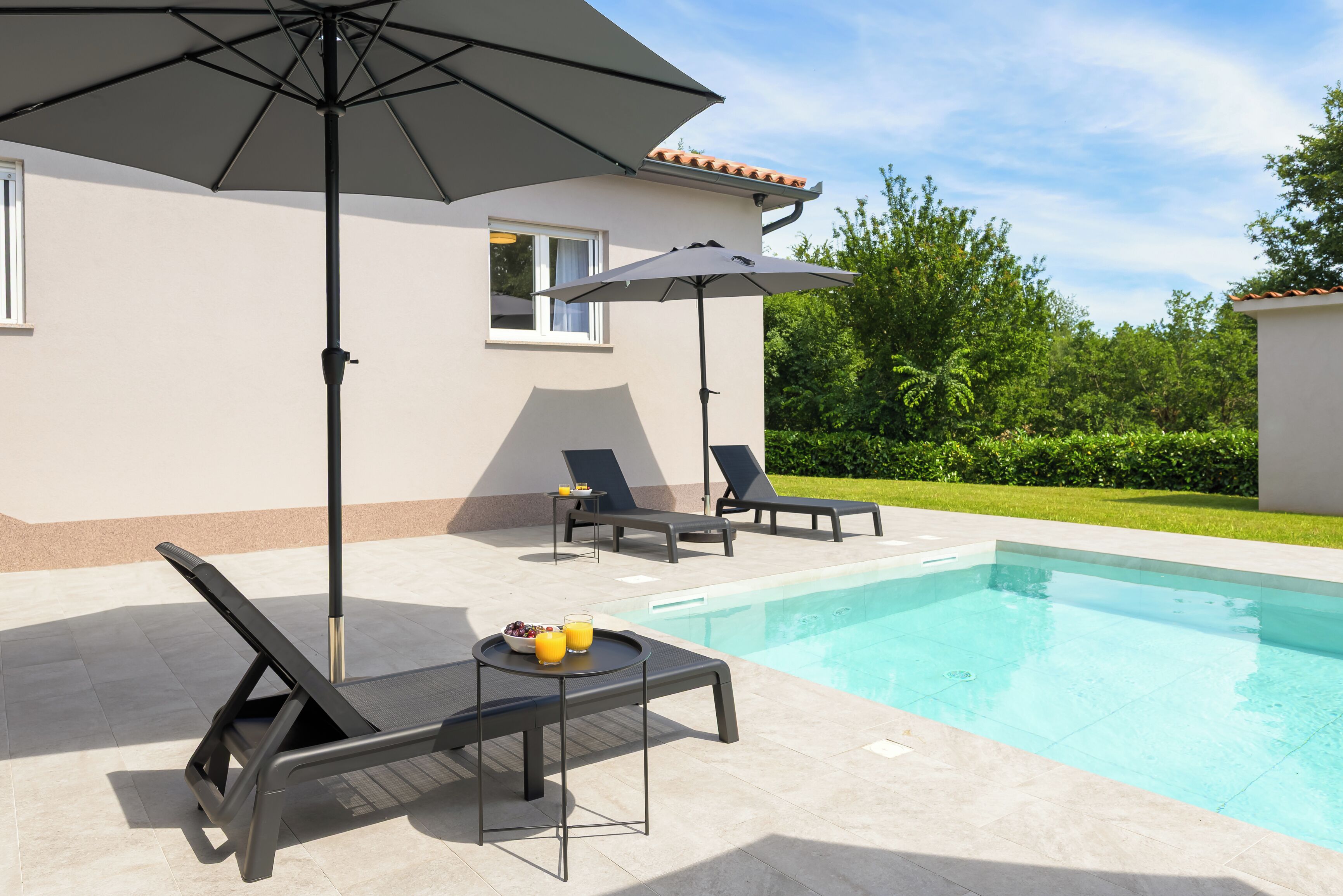 A swimming pool area with lounge chairs, a table with drinks, and umbrellas.