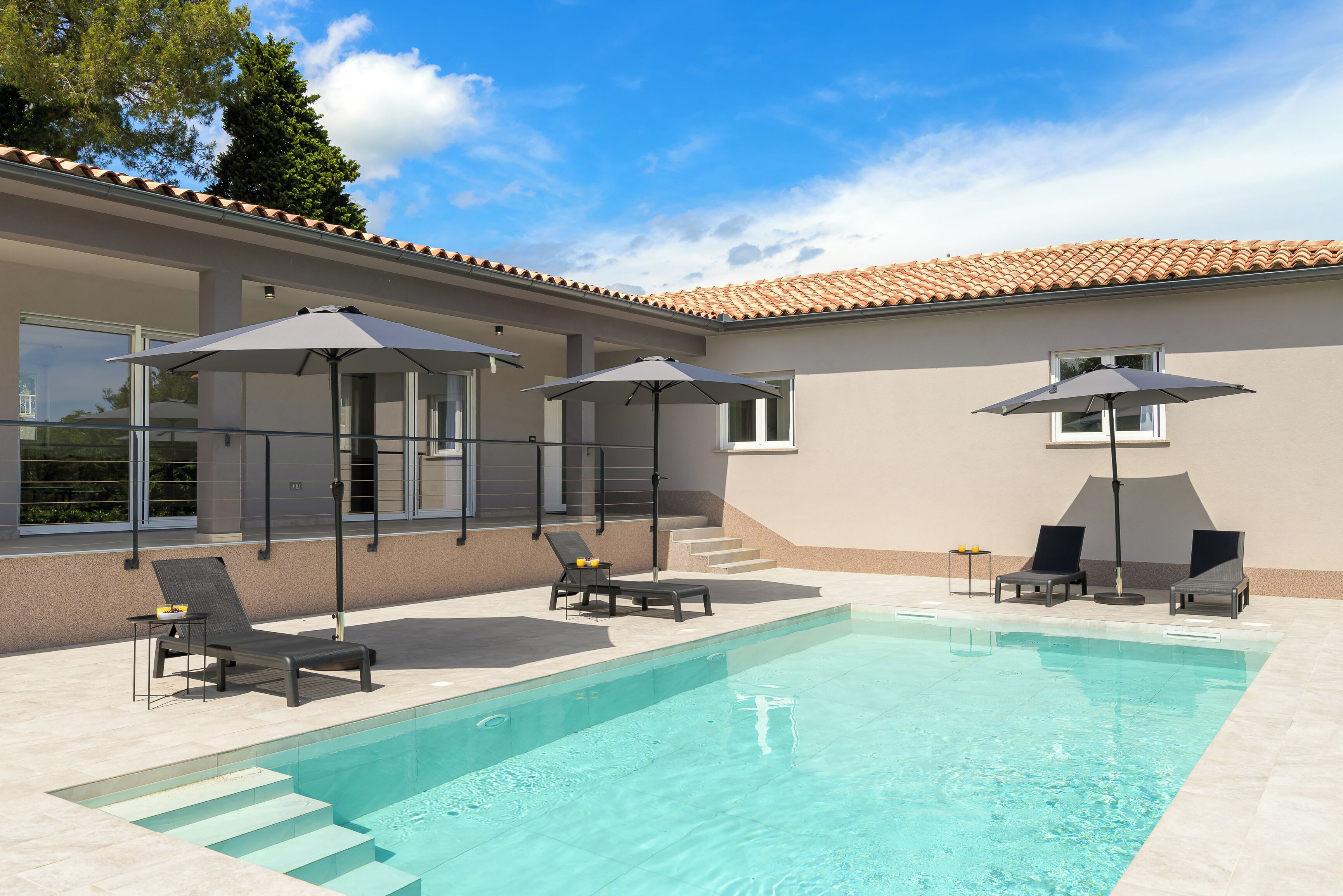 A swimming pool with lounge chairs and umbrellas, a tiled roof, and a clear sky.