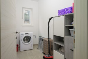 Een wasruimte met een wasmachine, een koffer en een stofzuiger.