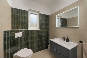A bathroom with a toilet, sink, mirror, and green-tiled walls. - Villa Zafira (Istria - Pula) (Pula)
