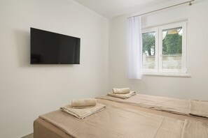 Een kamer met twee bedden, een flatscreen televisie, een raam met gordijnen en uitzicht op bomen.