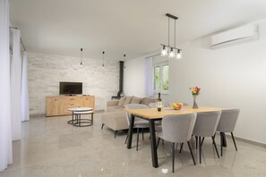 Ein modernes Wohnzimmer mit Fernseher, Sofa, Esstisch und Stühlen.