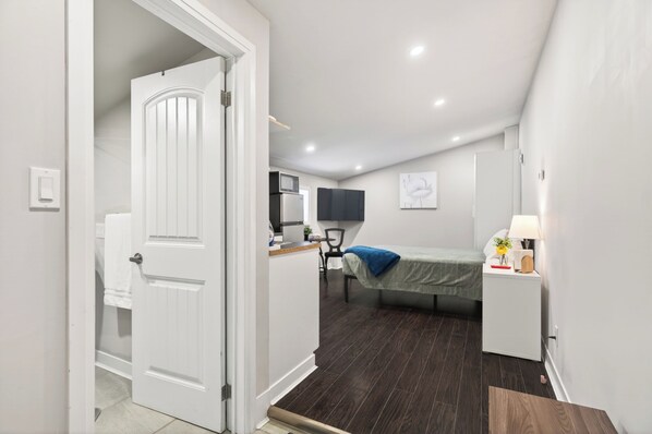 A bedroom with a bed, bedside table, lamp, and a small desk with a chair. - Cozy Studio w/ Parking | Heart of Ridgetown (Ridgetown)