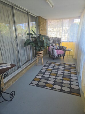 A room with a large window, a chair with a patterned cover, a potted plant, and a patterned rug.