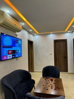 A conference room with a flat-screen TV displaying various apps, two dark chairs, a wooden table with rose petals, and a ceiling with recessed lighting. - Apartment center Gueliz (Marrakech)