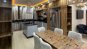 Eine moderne Küche mit integrierten Geräten, ein Essbereich mit Holztisch und weißen Stühlen sowie eine Wand mit Holzvertäfelung.