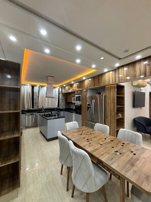 A modern kitchen with built-in appliances, a dining area with a wooden table and white chairs, and a wooden accent wall. - Apartment center Gueliz (Marrakech)