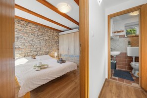 Ein Schlafzimmer mit Steinwand, Holzbalken, einem Bett mit Handtüchern und einem Kleiderschrank.