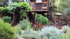 A wooden cabin with a balcony, surrounded by a garden with various plants and flowers. - Tranquil Country Estate with Fantastic Garden (Glen Ellen)