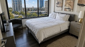 Quarto moderno com uma janela grande, uma cama, uma escrivaninha e uma cadeira.