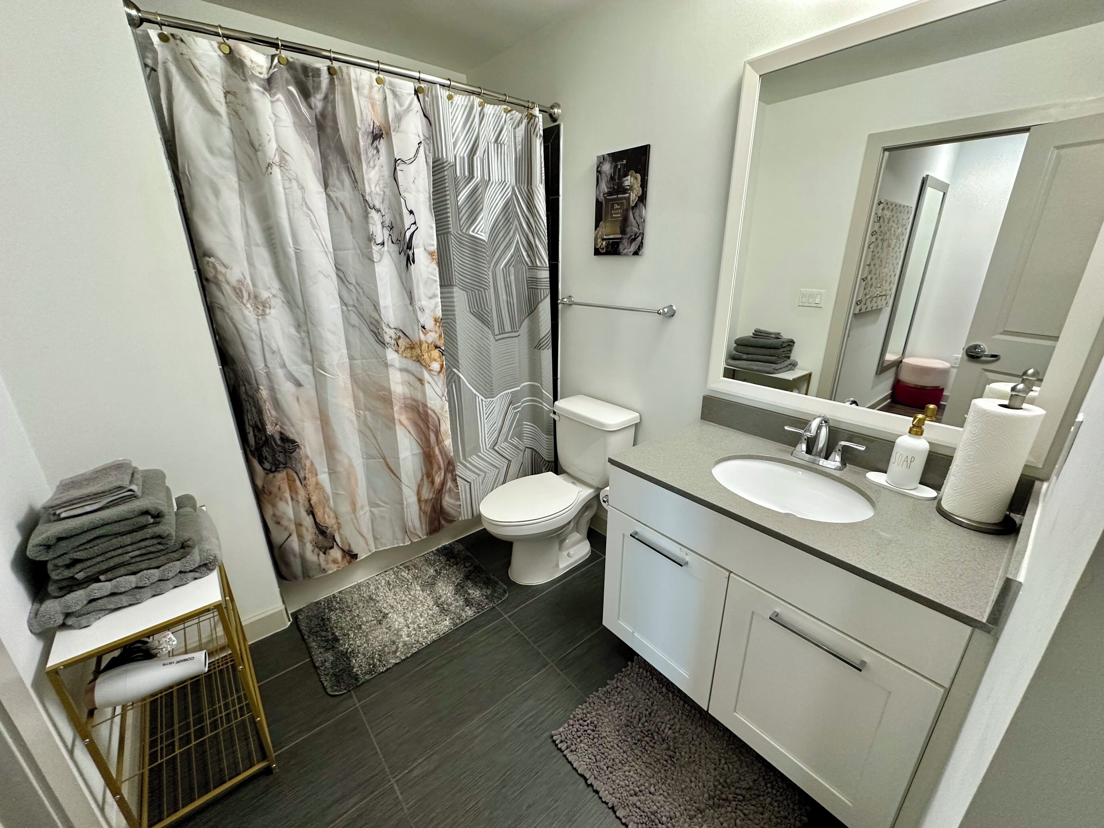 A bathroom with a shower curtain, toilet, sink, and mirror.