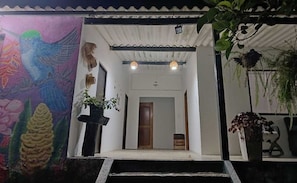 Entrada de un edificio con un mural colorido, una puerta de madera y plantas en macetas.