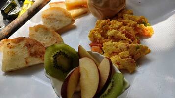 Un plato de desayuno con tostadas, huevos revueltos y fruta cortada.