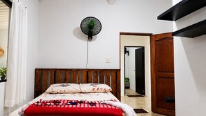 Una camera da letto con un letto, una ventola a parete, una testiera in legno, una porta e uno specchio.