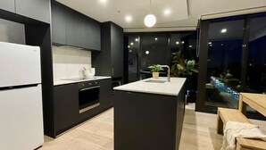 A modern kitchen with a central island, built-in oven, and a view of the city at night. - The Webster in the City (Reid)