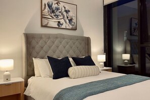 Ein Schlafzimmer mit einer gesteppten Kopfteil, einem Bett mit weißer und dunkelblauer Bettwäsche, zwei Nachttischlampen und einem Bild über dem Bett.