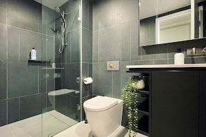 Ein modernes Badezimmer mit einer Duschkabine, Toilette, Waschbecken mit Spiegel und einer Topfpflanze.