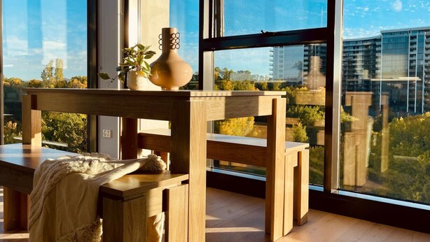 A modern interior with a wooden table and chairs, a vase with flowers, and a view of buildings through large windows. - The Webster in the City (Reid)
