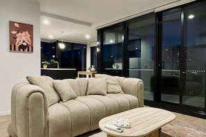 Ein modernes Wohnzimmer mit einer Couch und einem Couchtisch, im Hintergrund ein Küchenbereich und eine große Schiebeglastür.