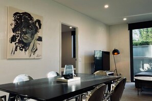 Ein moderner Essbereich mit einem langen Tisch, Stühlen, einem großen abstrakten Gemälde, einem Kühlschrank und einer Stehlampe.