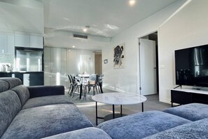 Una sala de estar moderna con un sofá, una mesa de comedor con sillas, un televisor y un cuadro en la pared.