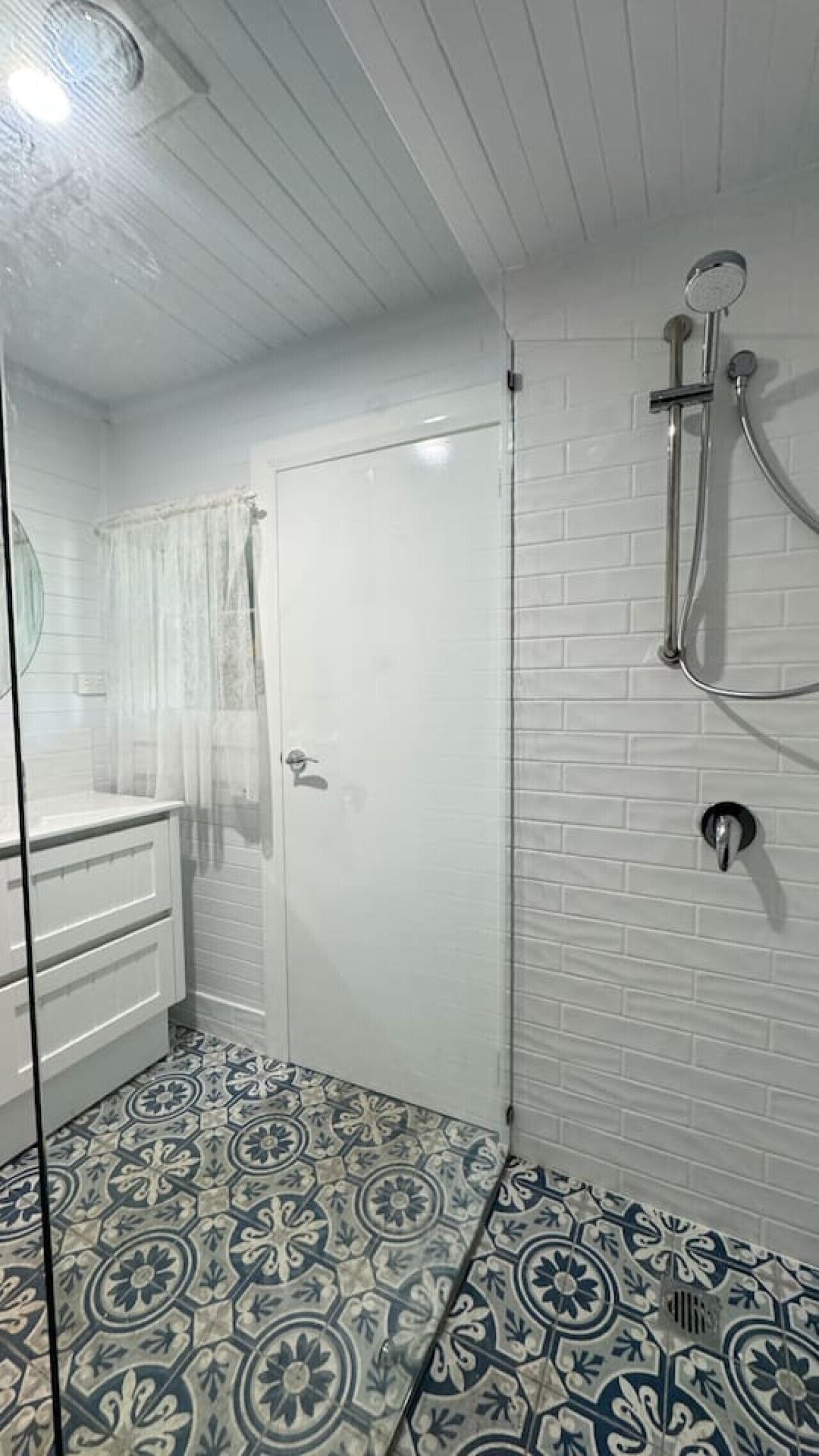 Ein Badezimmer mit Dusche, Glastür, weiß geflieste Wand und dekorativen Bodenfliesen.