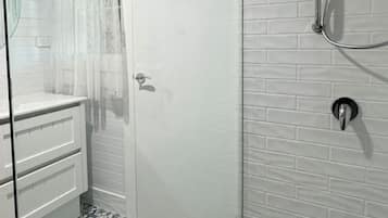 Ein Badezimmer mit Dusche, Glastür, weiß geflieste Wand und dekorativen Bodenfliesen.