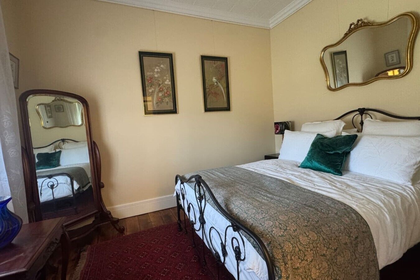 Ein Schlafzimmer mit einem Bett, einem Spiegel, zwei gerahmten Bildern an der Wand und einem roten Teppich.