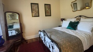 A bedroom with a bed, a mirror, two framed pictures on the wall, and a red rug.