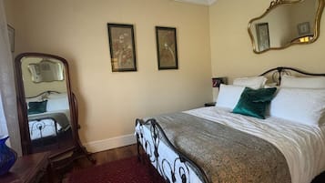 Ein Schlafzimmer mit einem Bett, einem Spiegel, zwei gerahmten Bildern an der Wand und einem roten Teppich.