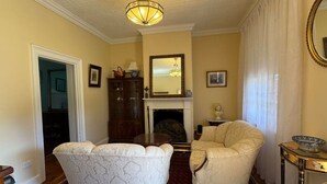 A living room with a fireplace, a chandelier, a large mirror, and a dining table.