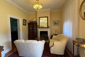 Una sala de estar con chimenea, candelabro, un espejo grande y una mesa de comedor.