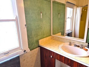 Un baño con un lavamanos blanco, un espejo y una pared verde.