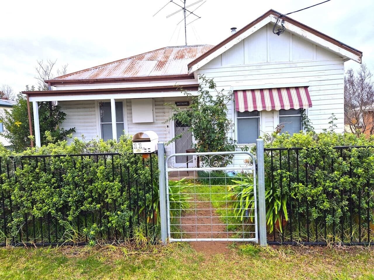 Una casa de dos pisos con un portón de metal, un pequeño jardín y un buzón.