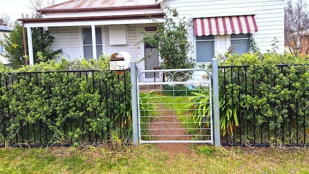 Ein zweistöckiges Haus mit einem Metallzaun, einem kleinen Garten und einem Briefkasten.