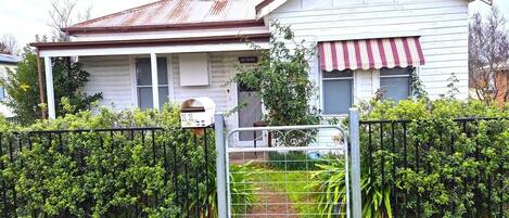 Una casa de dos pisos con un portón de metal, un pequeño jardín y un buzón.