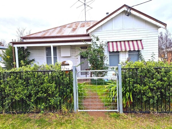 Una casa de dos pisos con un portón de metal, un pequeño jardín y un buzón.
