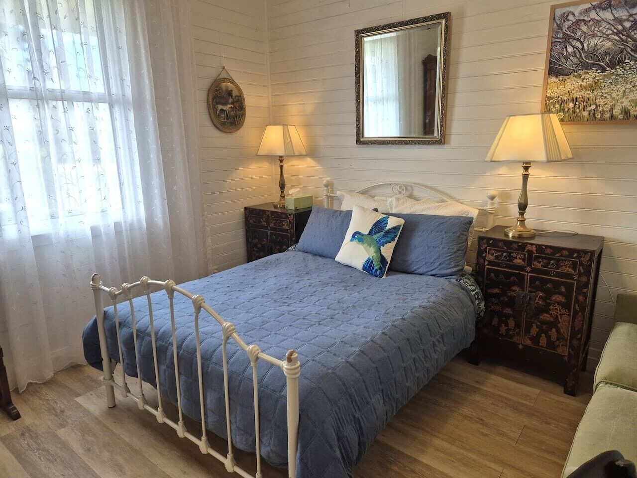 A bedroom with a bed, two bedside tables, a mirror, and a window with curtains.