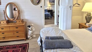 Ein Schlafzimmer mit einem Bett, einem Schminktisch, zwei Spiegeln, einer Hundefigur und einem Gang zu einem weiteren Raum.
