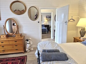 Un dormitorio con cama, cómoda, dos espejos, una estatua de perro y un pasillo que conduce a otra habitación.