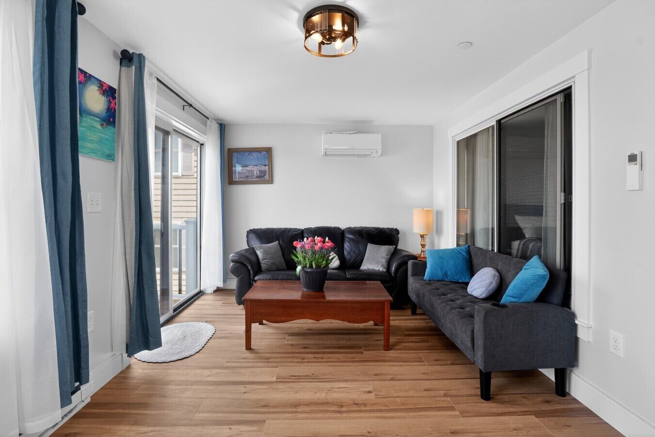 Een woonkamer met een bank, een bijzettafeltje met bloemen, een lamp en een schilderij aan de muur.