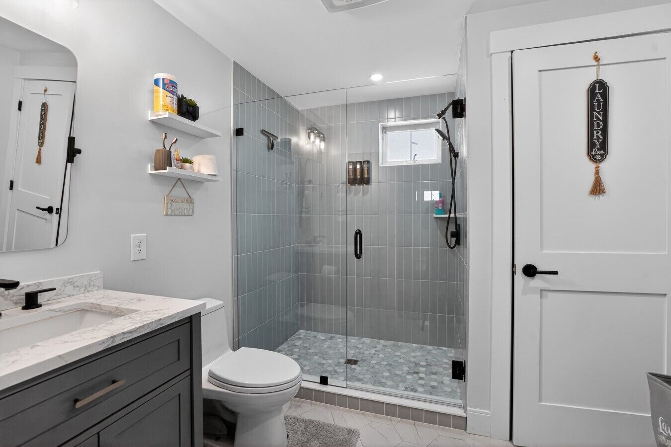 A modern bathroom with a glass-enclosed shower, a toilet, and a vanity with a marble countertop.