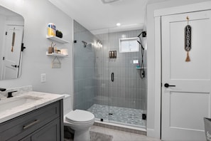 A modern bathroom with a glass-enclosed shower, a toilet, and a vanity with a marble countertop.
